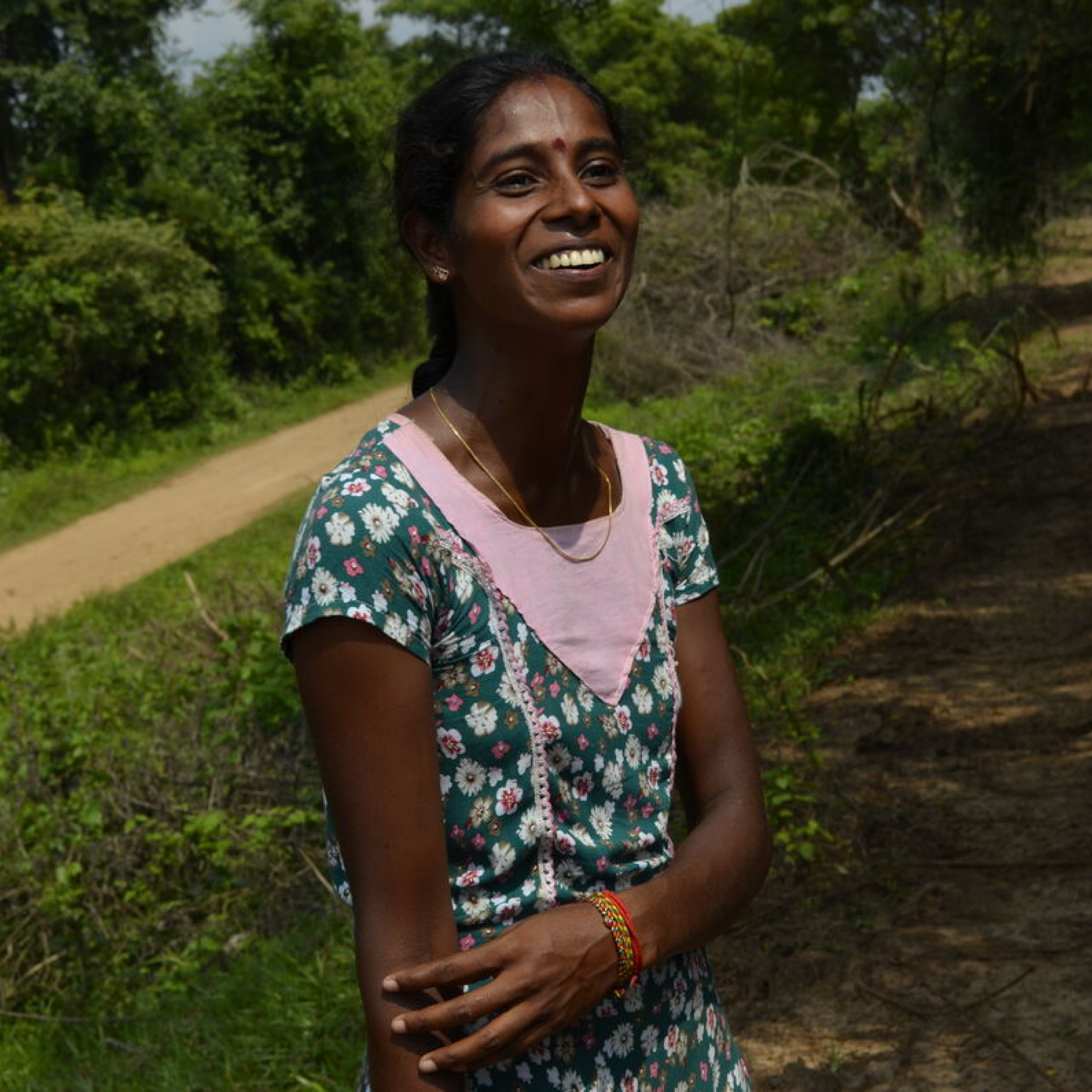 a young women from Sri Lanka, smiling, wearing a green and purple dress. Behind a park with a walking path