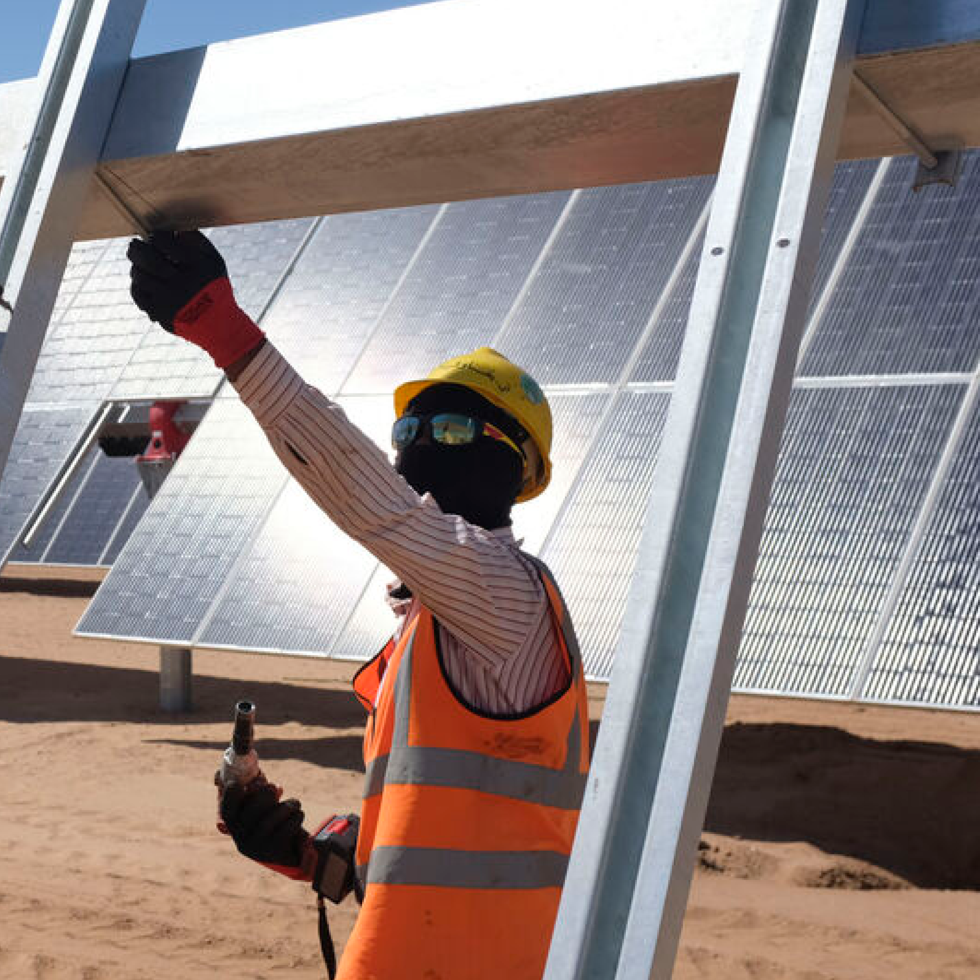 A man wearing protection orange jacket, yellow had and glasses is checking solar panels