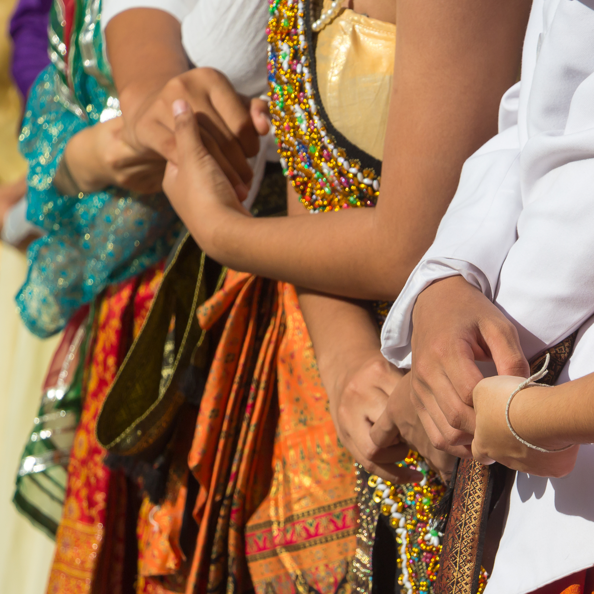 Photograph of arms and hands. Hands are holding one another. Clothes are colorful.