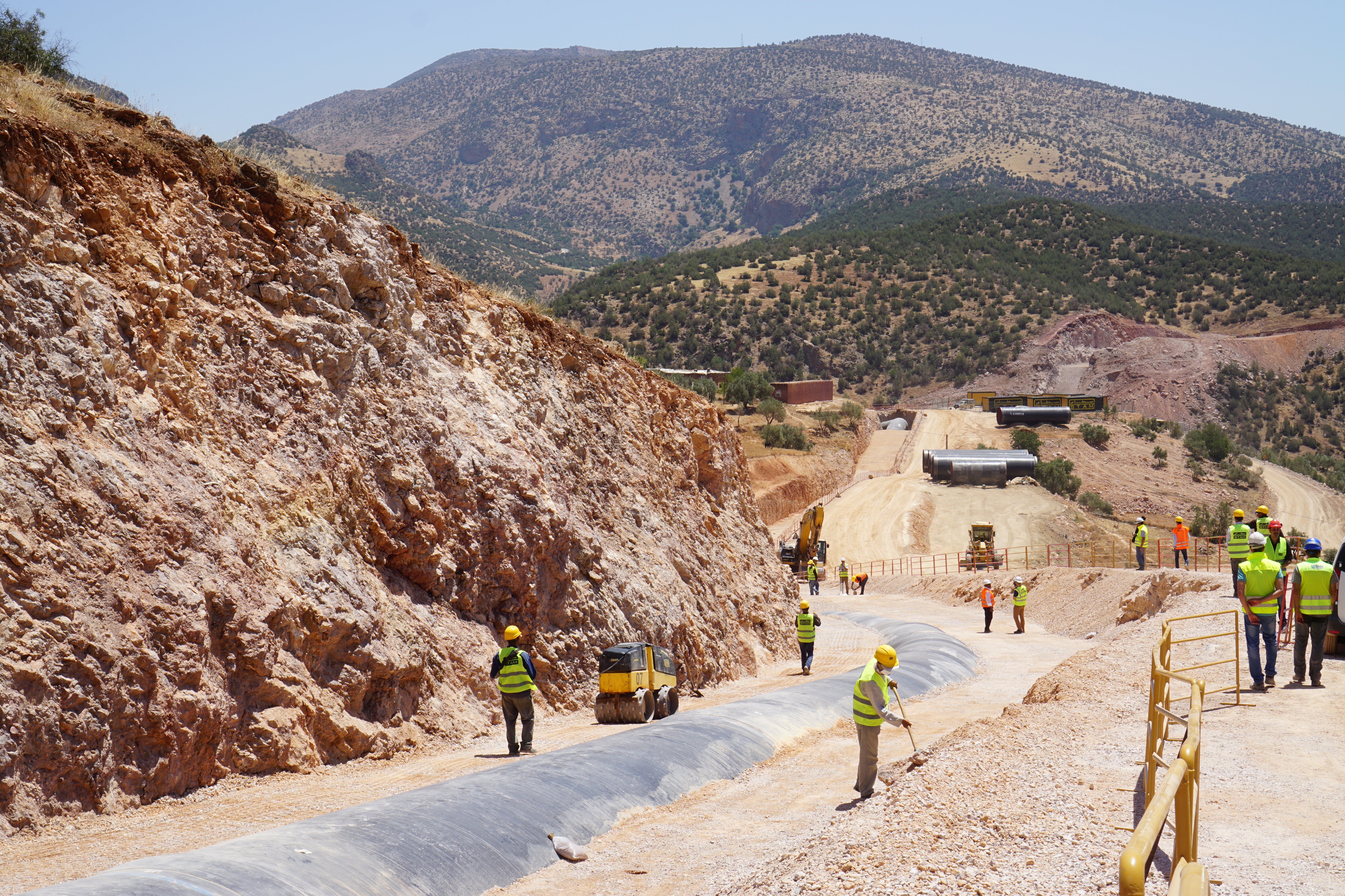Workers installing pipeline infrastructure along a dirt road in a mountainous, arid landscape, Morocco (Project FP043).