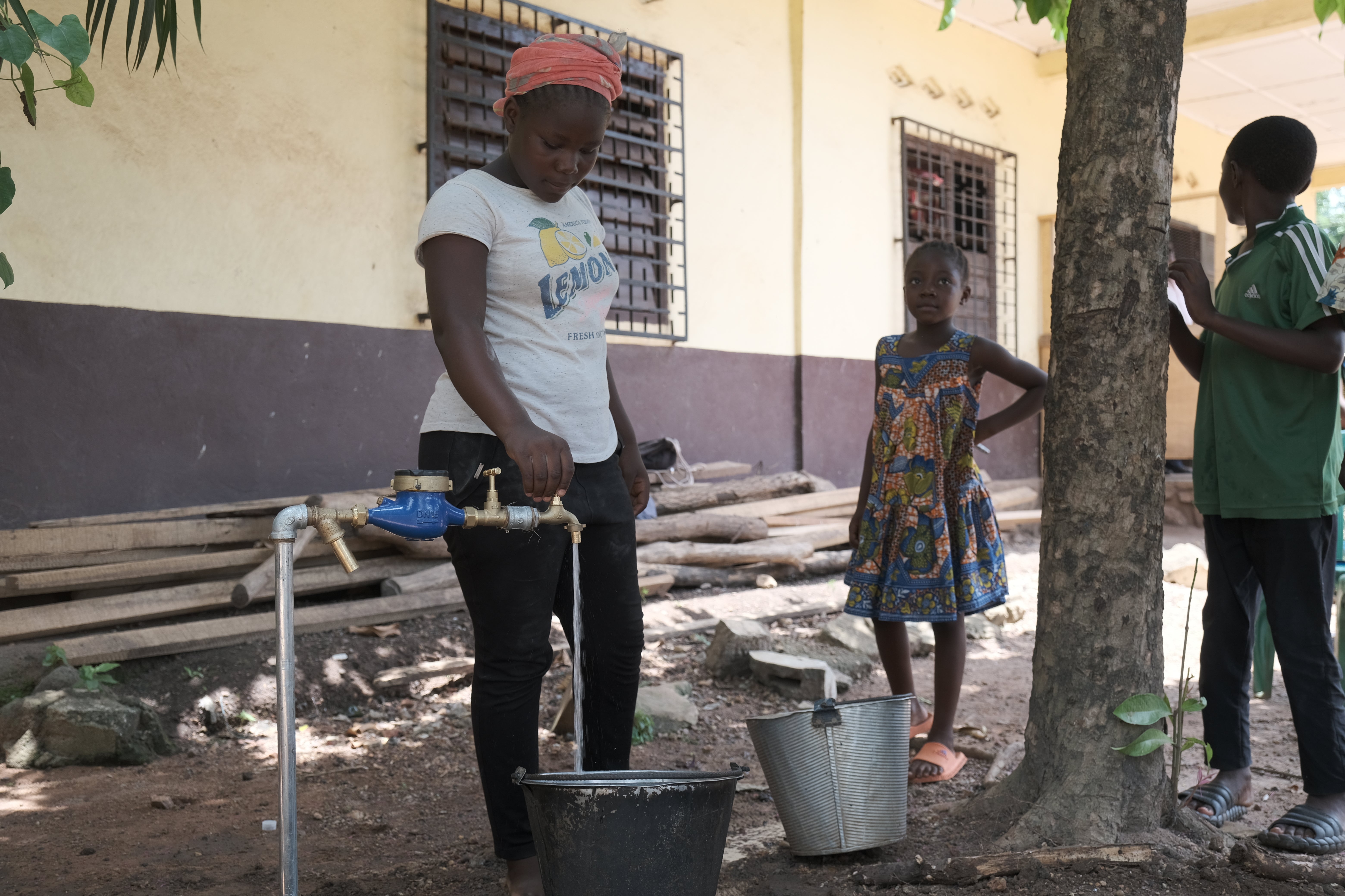 A girl is filling a bucket of water from a tap in the street.
