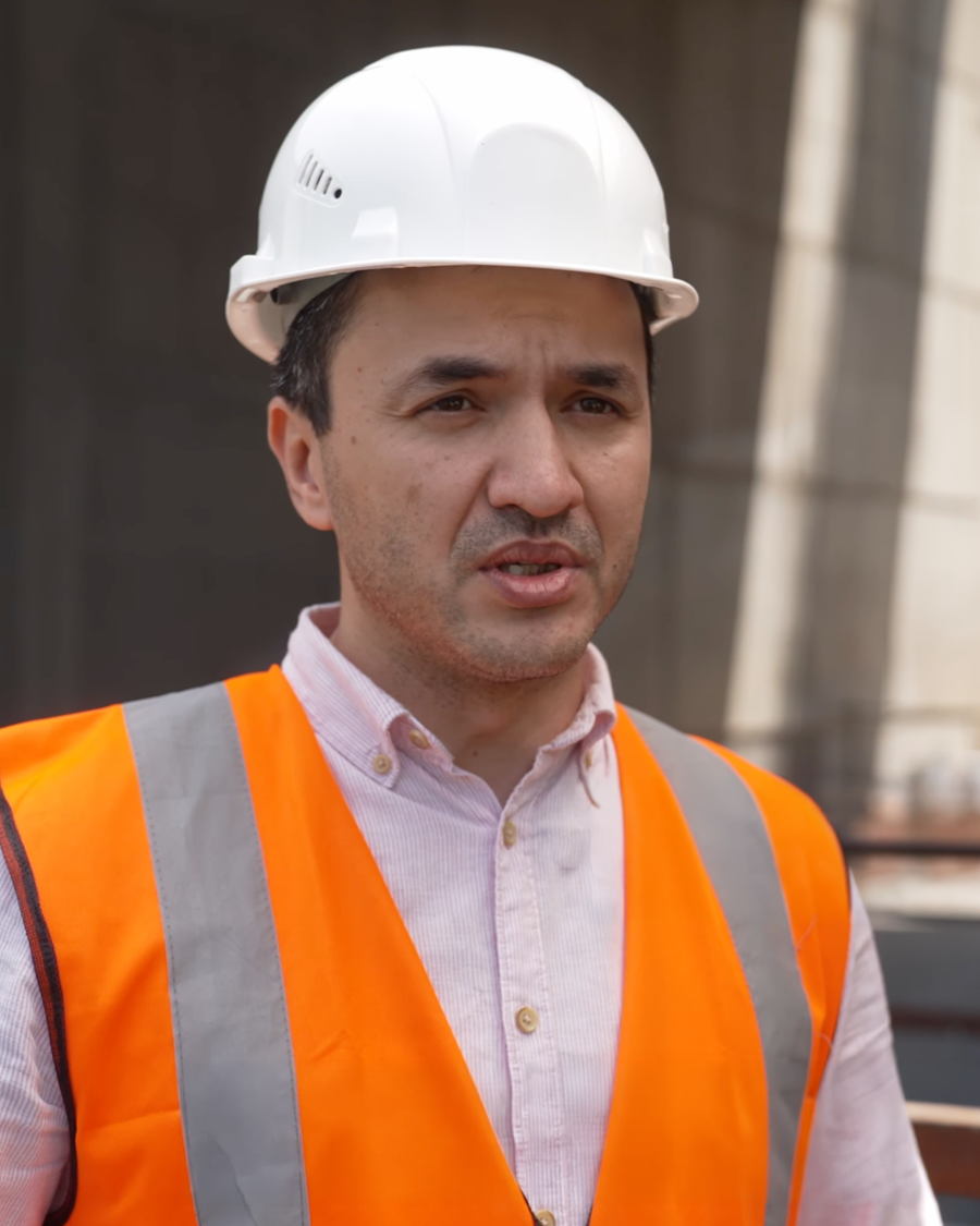 Construction worker wearing a white hard hat and orange safety vest at an outdoor worksite