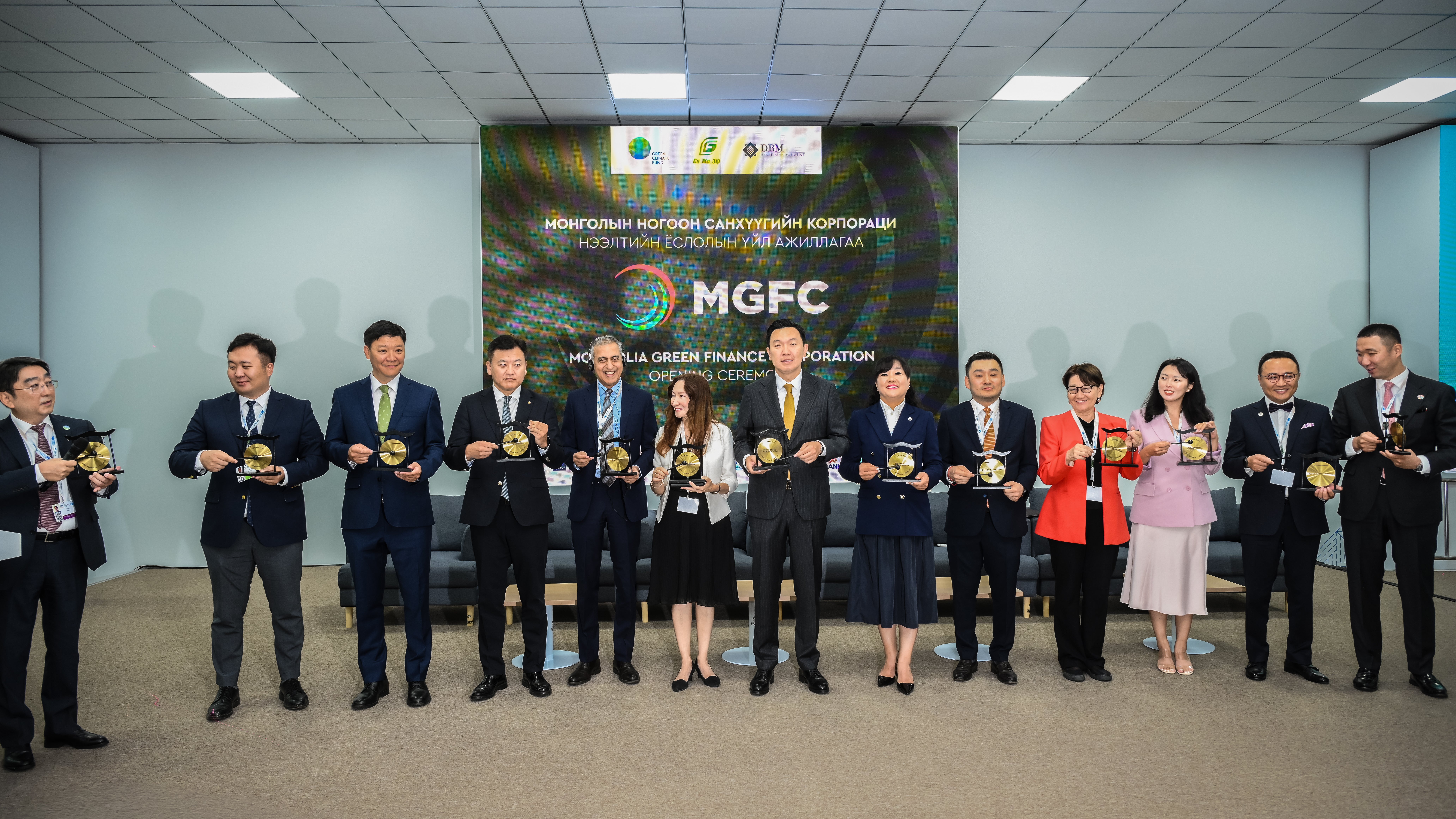 Group of attendees standing on a stage during the MGFC (Mongolia Green Finance Corporation) opening ceremony, each holding a commemorative plaque in front of a large event backdrop.