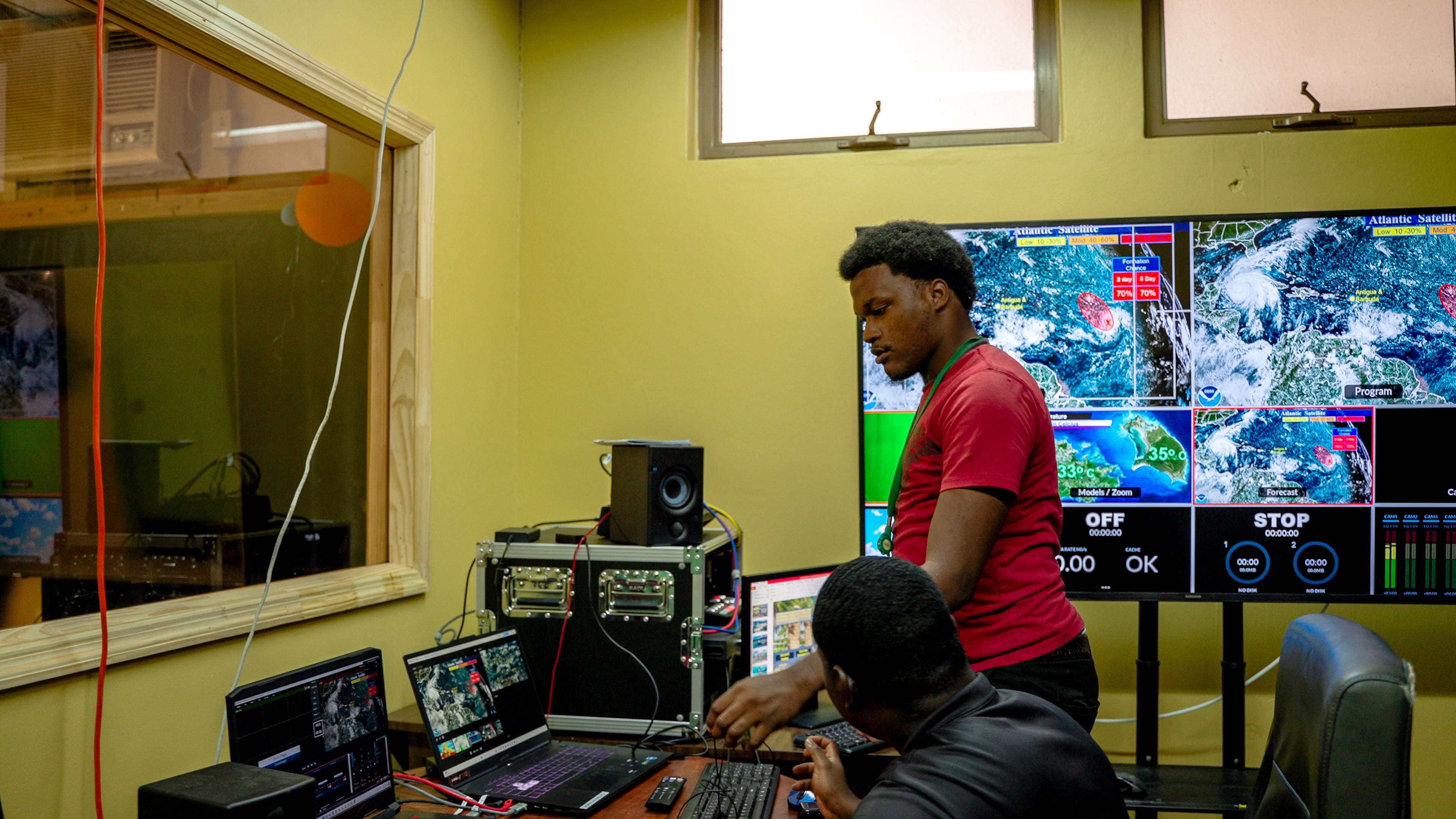 Staff operating weather monitoring and forecasting systems in a control room with multiple satellite displays and computer workstations