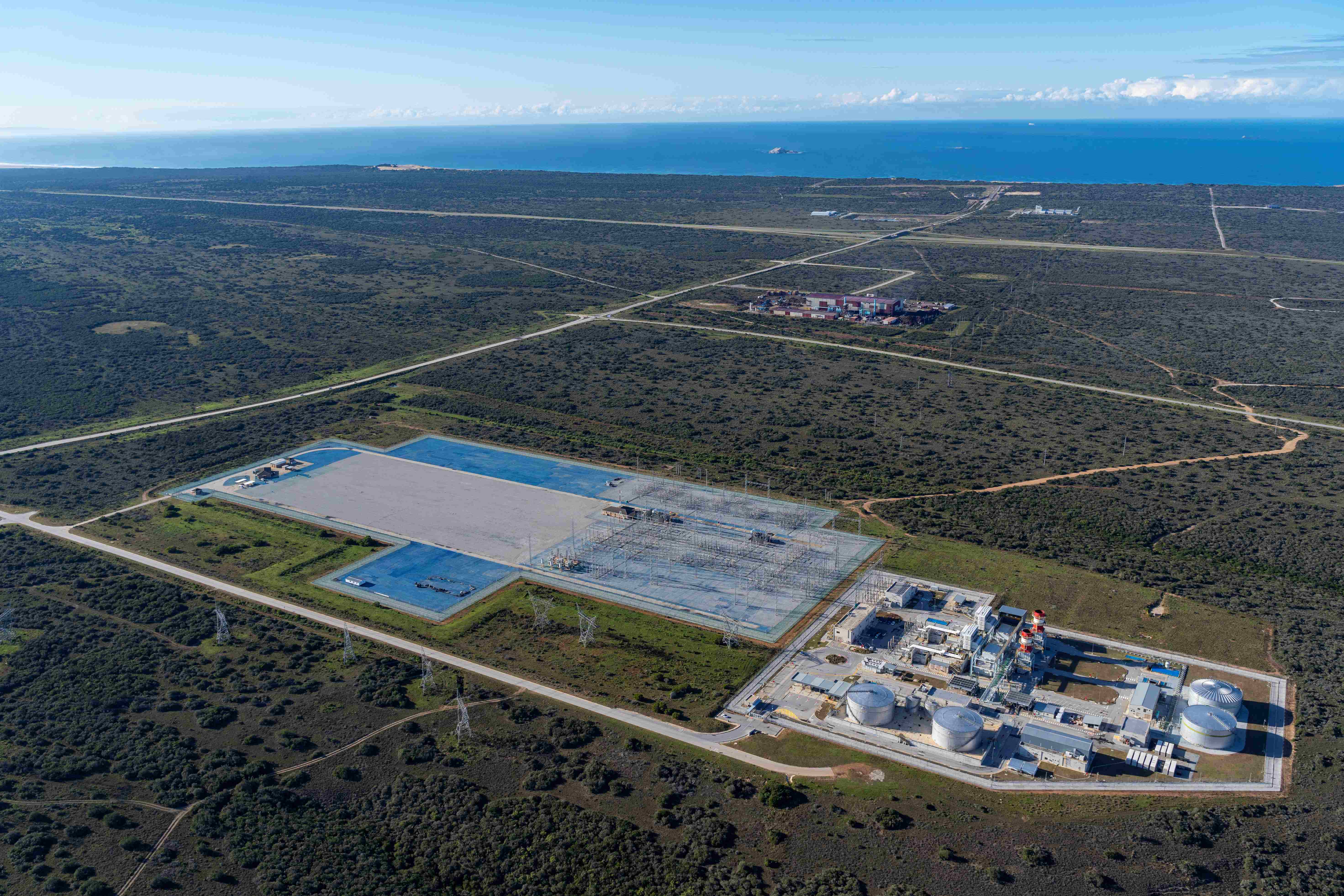 Aerial view of an industrial power facility surrounded by vegetation and roads near the coast.