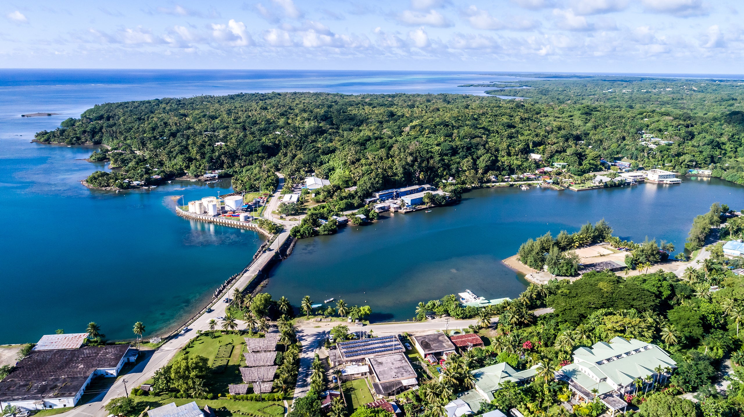 Aerial view of a lush tropical coastal community surrounding a sheltered bay, with roads and buildings among dense vegetation.