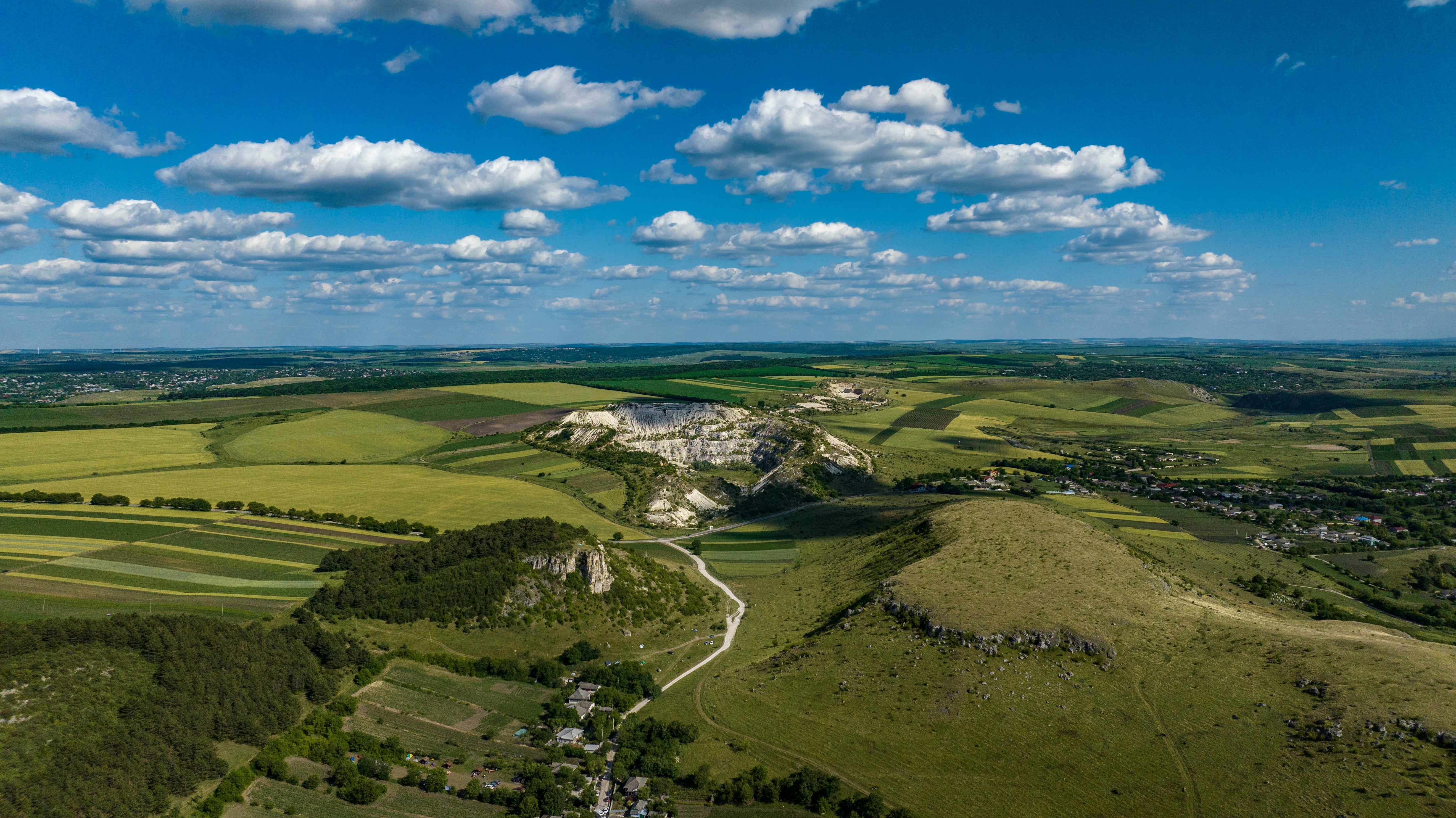 Aerial view of rolling farmland, rocky hills and small settlements beneath a bright blue sky with scattered clouds.