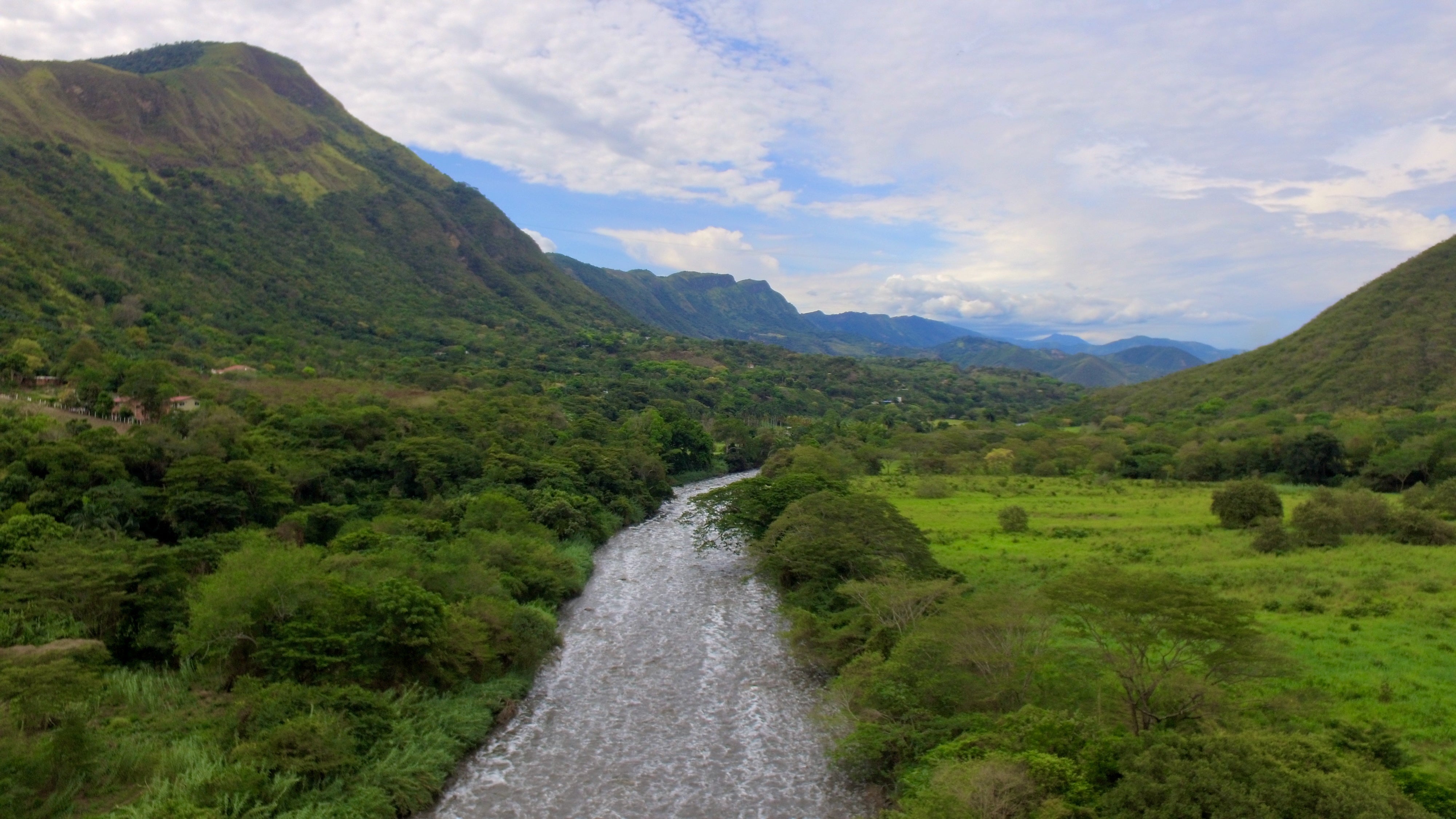 River winding through a lush green valley surrounded by steep, forested mountains.