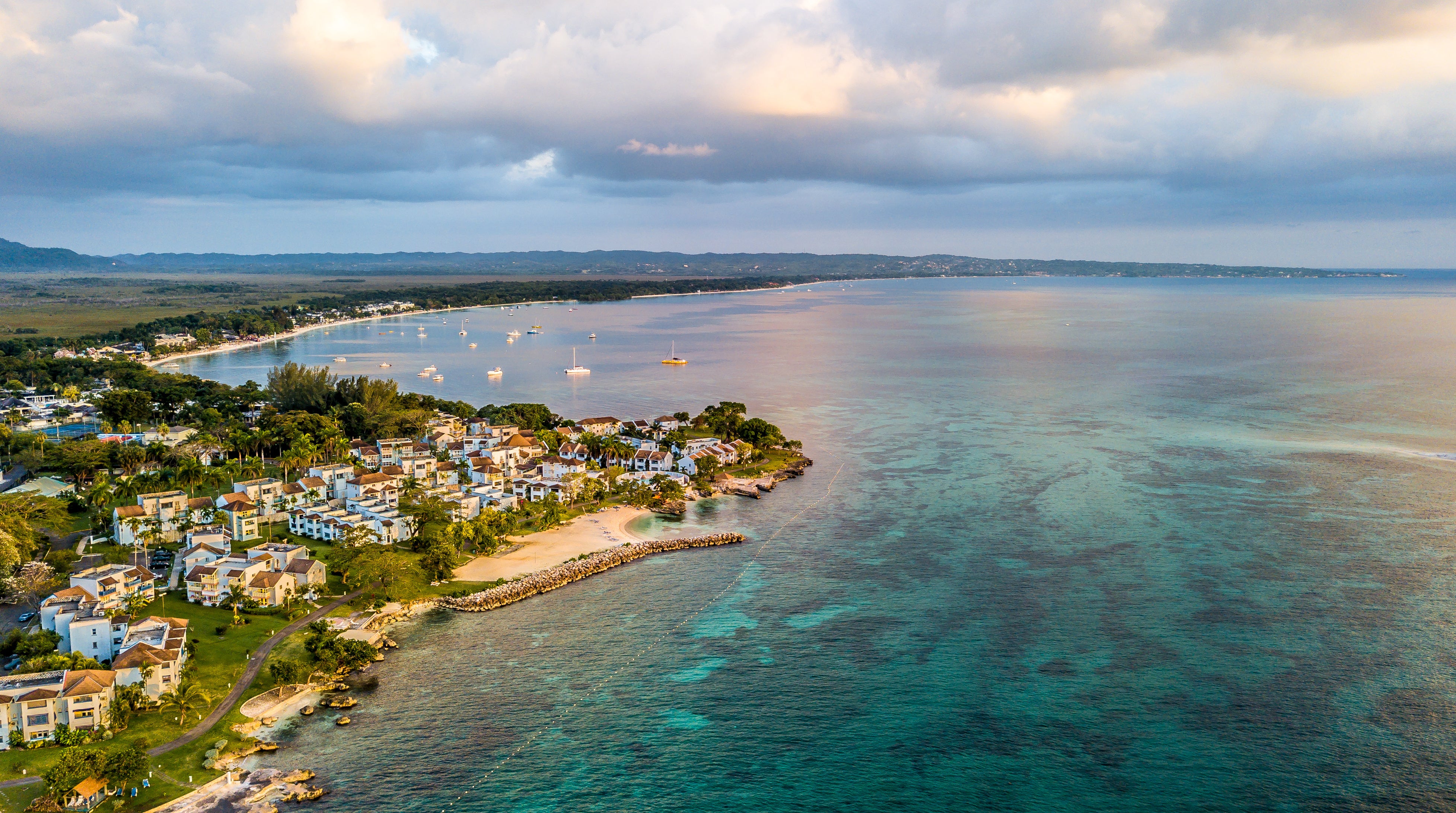 Aerial view of a coastal community beside turquoise water, with boats anchored offshore.