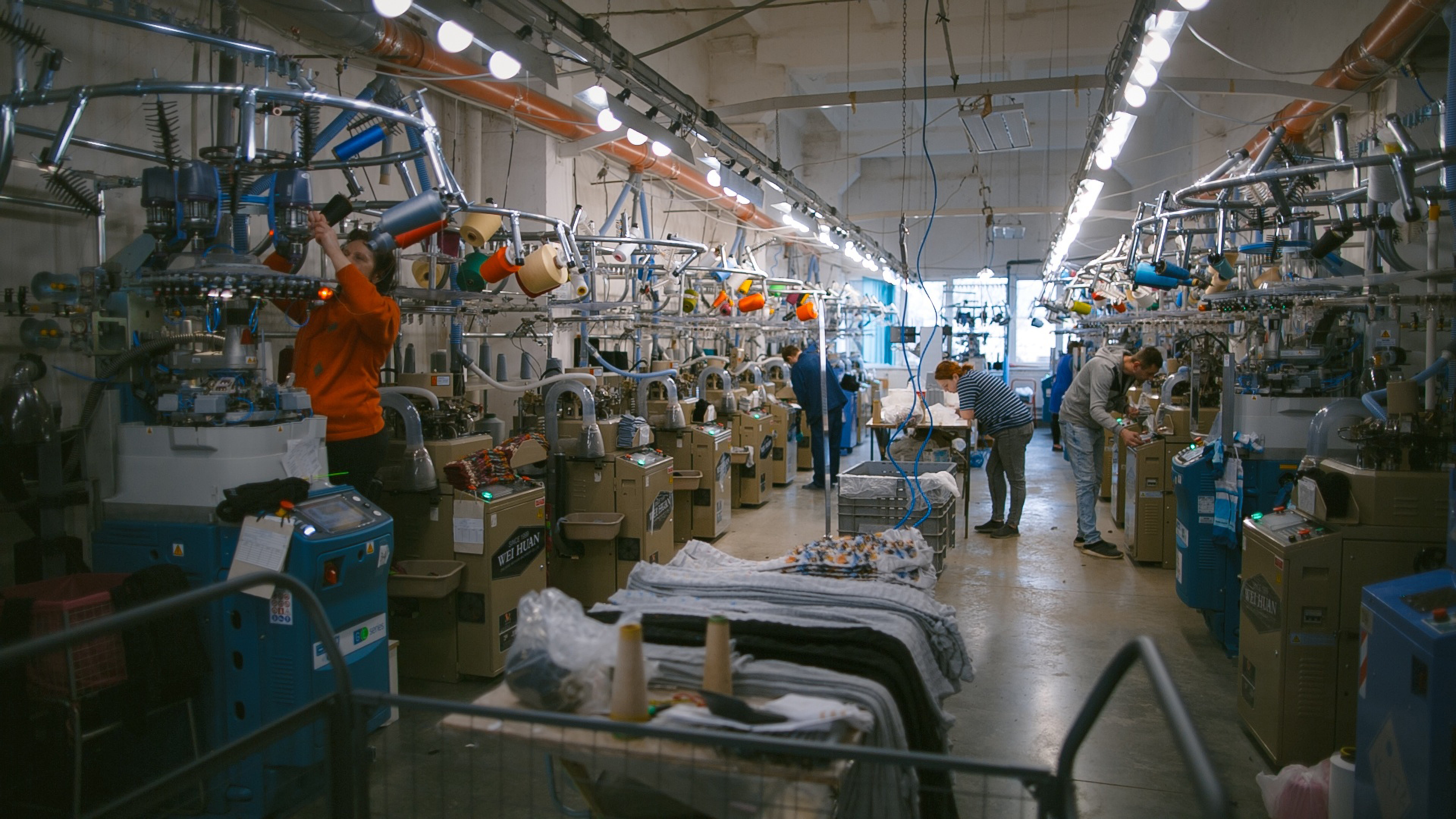 Workers operating rows of textile manufacturing machines inside a factory.